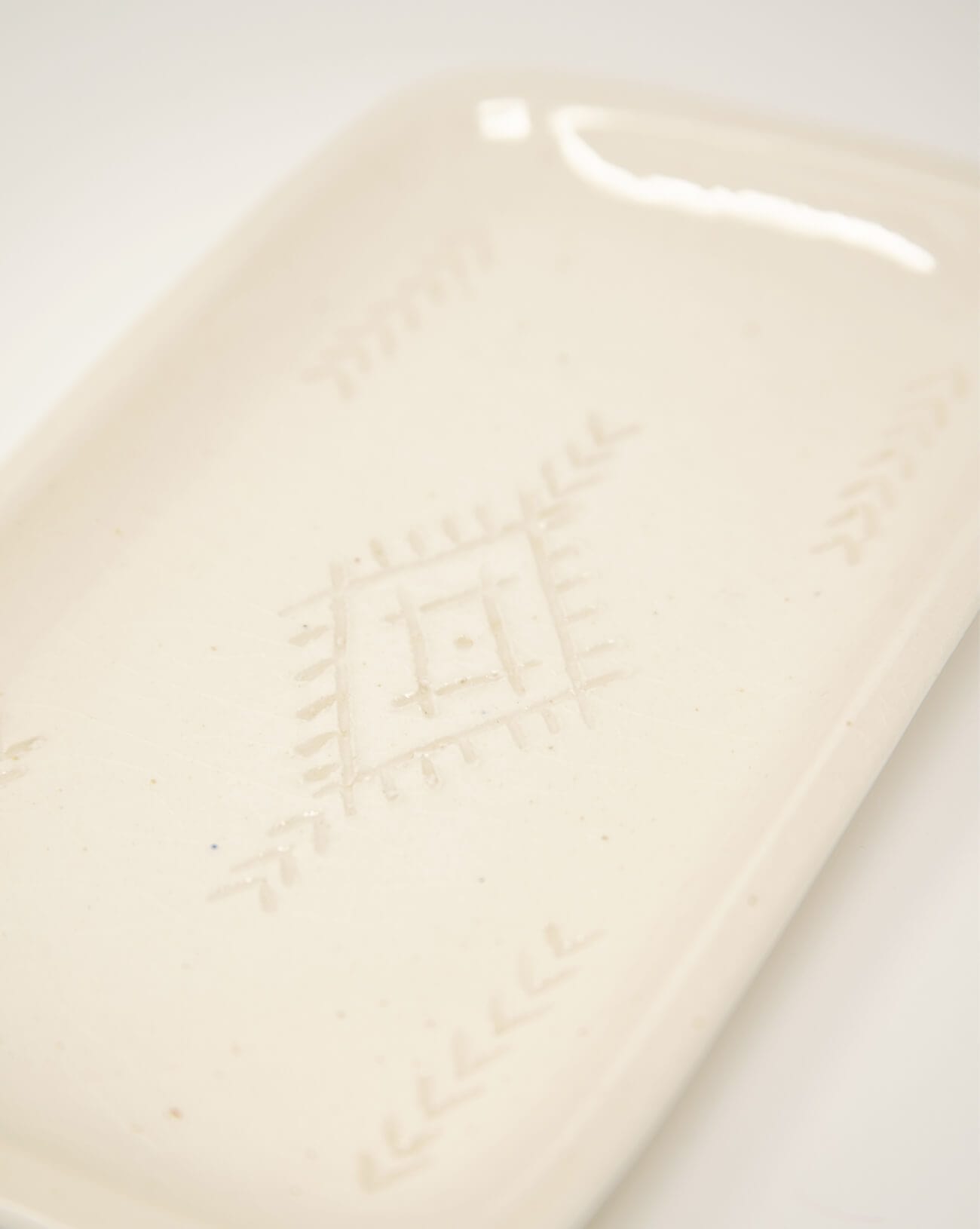 close up of white rectangle ceramic soap tray with designs in the center on a white background