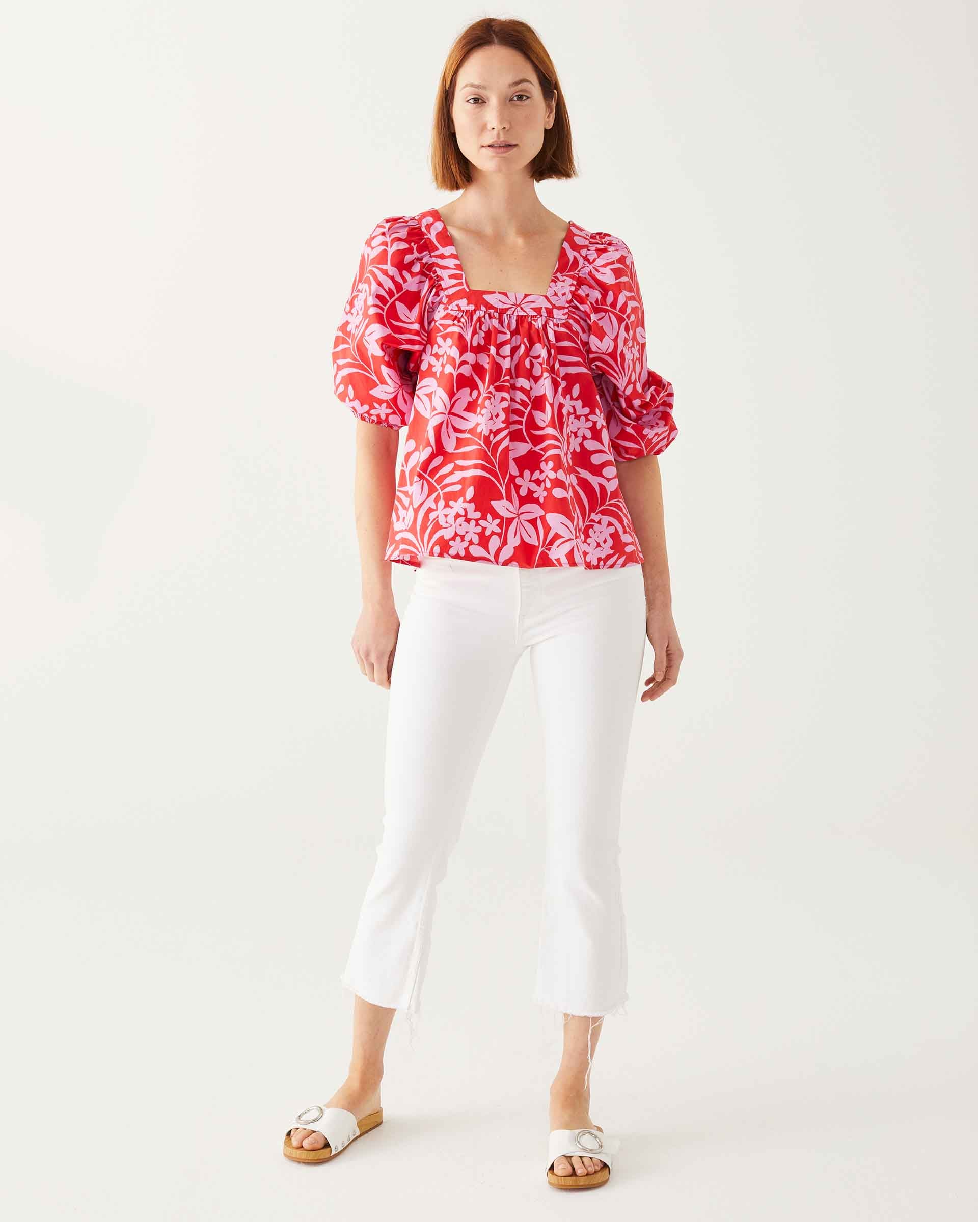 female wearing red top with pink floral print and puff sleeves standing on a white background