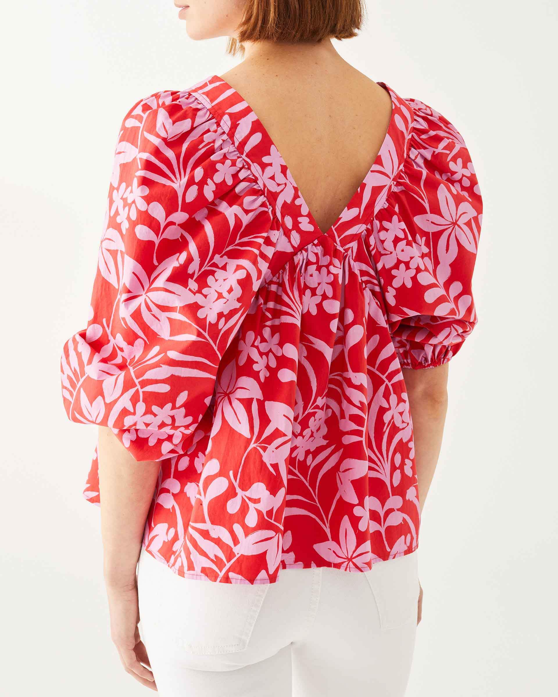 back close up of female wearing red top with pink floral print puff sleeves on white background