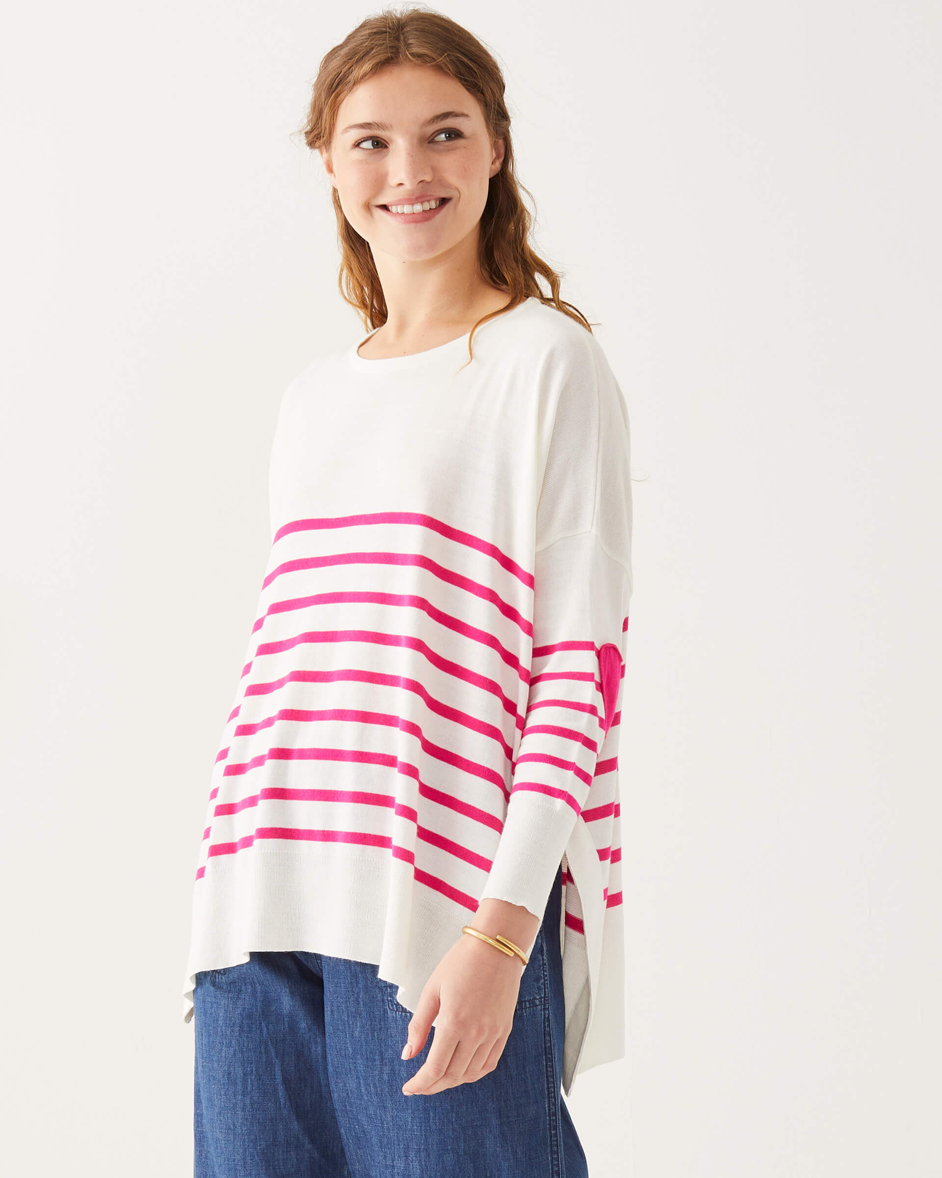 curly haired female wearing white and pink striped sweater standing on a white background 