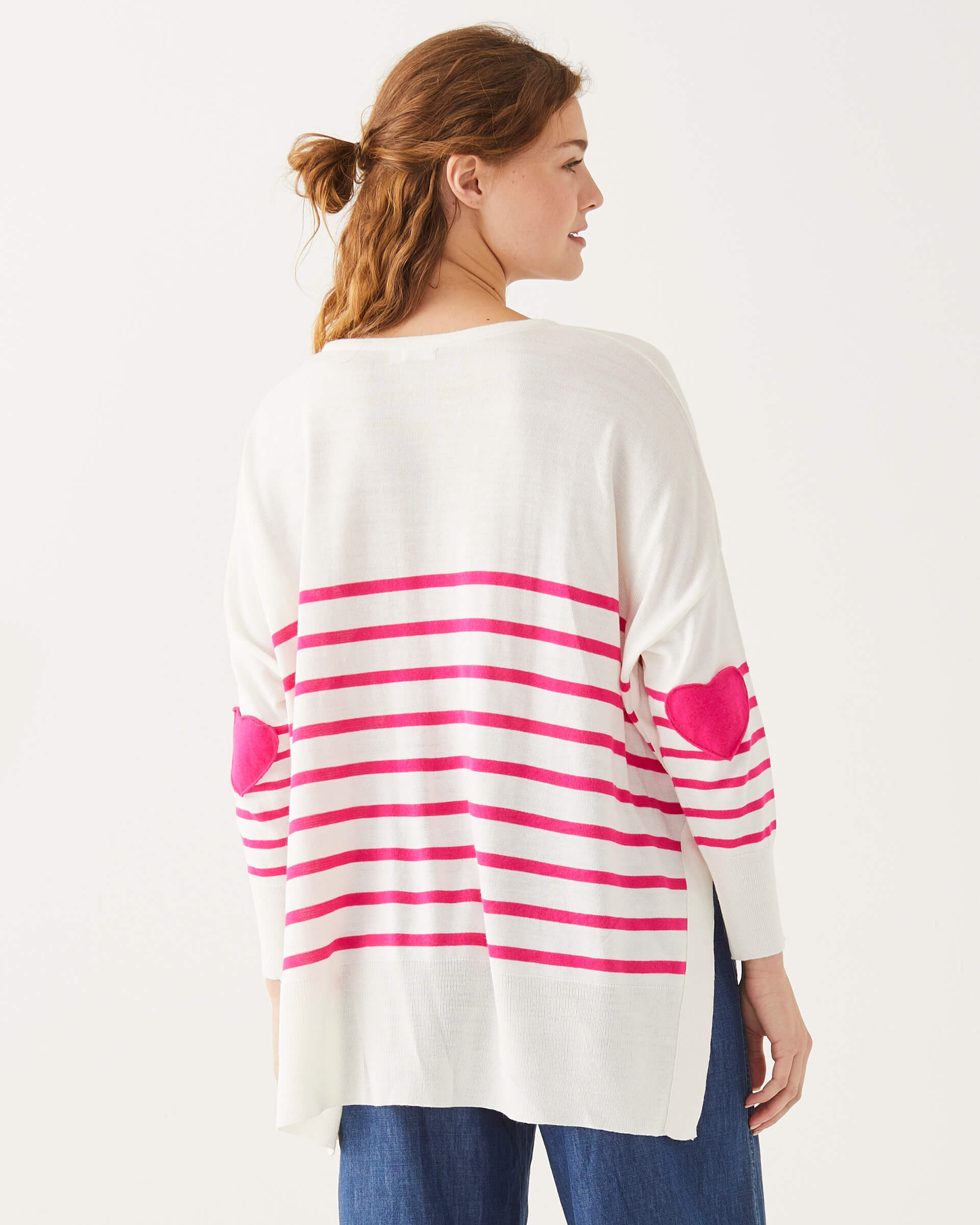 female wearing white and pink striped sweater with pink hearts on the elbow standing backwards