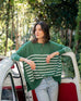 brunette female wearing green and white striped sweater leaning on an open car door