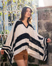 female wearing black and white striped v-neck poncho standing near a white gate outside 