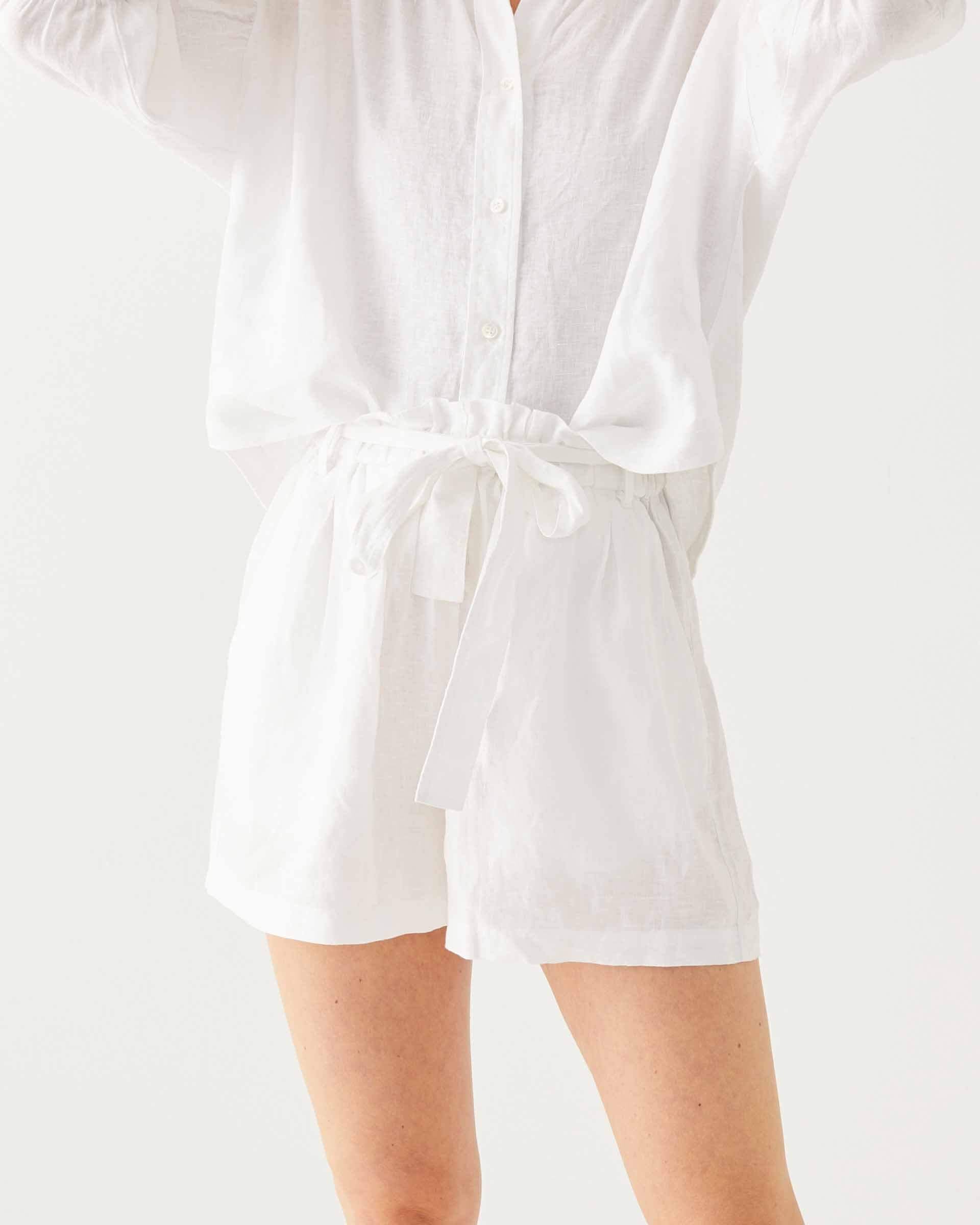close up of female wearing white linen shorts with belt and matching top on a white background