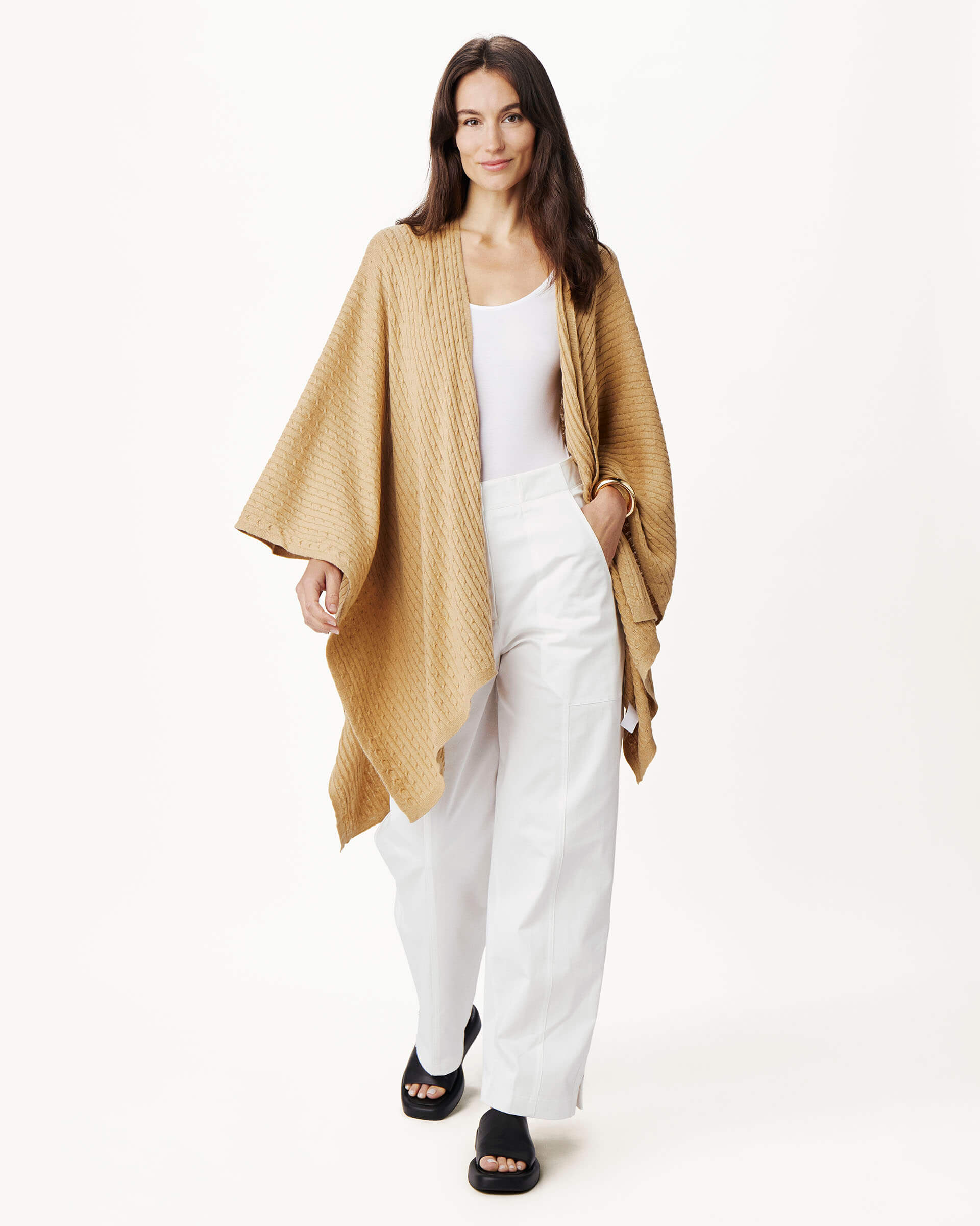 female wearing golden brown cable knit wrap with a hand in a pocket on a white background