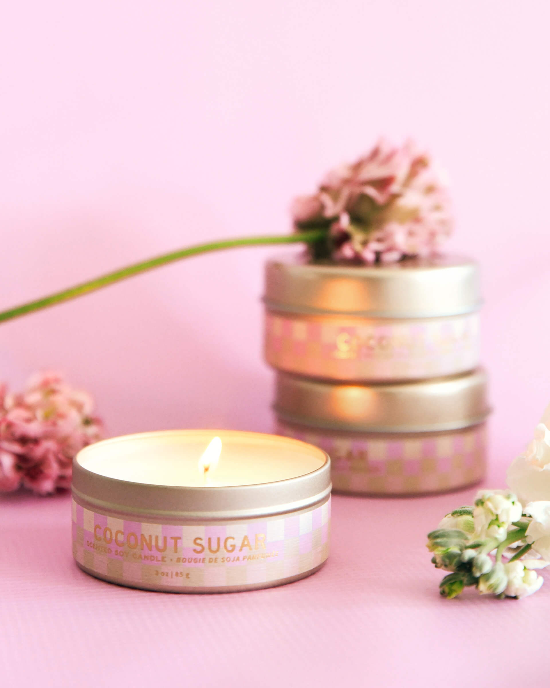 pink and white check 3 oz tin coconut sugar lit candle surrounded with flowers on pink background