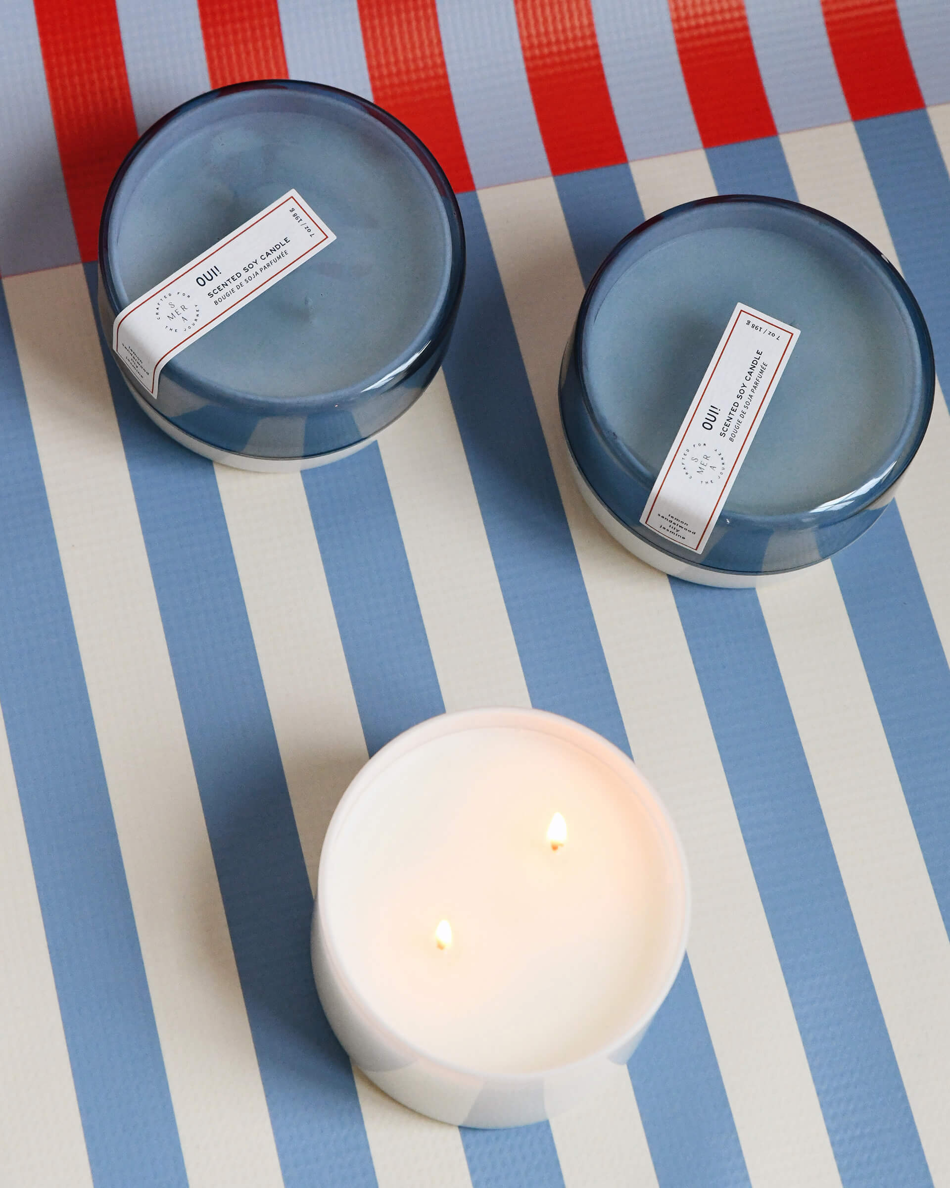 three 7 oz dark blue OUI! canister candles on a blue white and red striped background