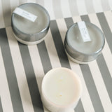 three 7 oz grey saltaire canister candles on a grey and white striped background