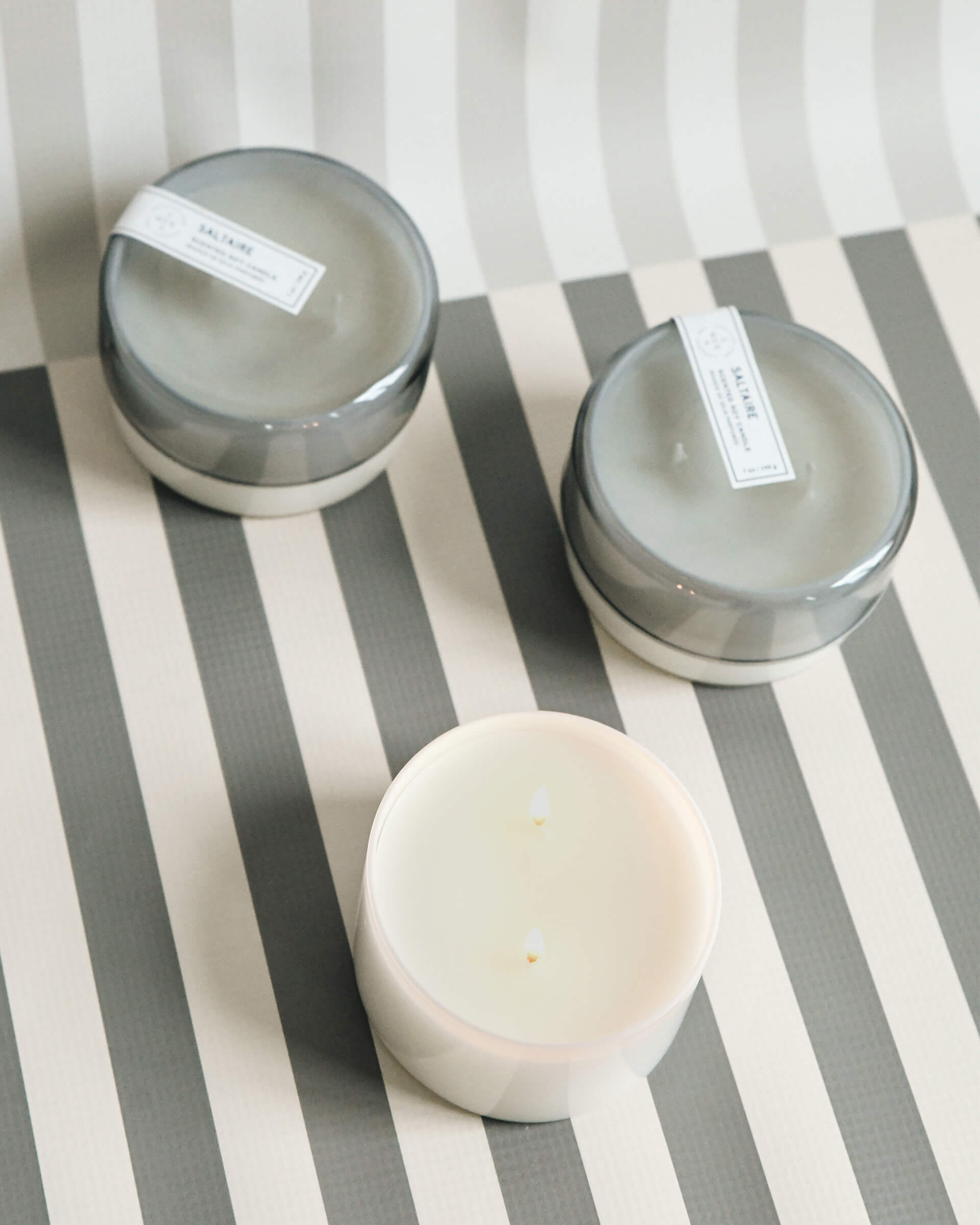 three 7 oz grey saltaire canister candles on a grey and white striped background