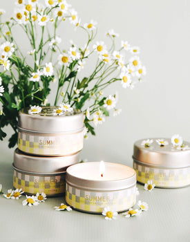 four yellow and grey checkered 3 oz tin summer day candles with white flower vase on grey background