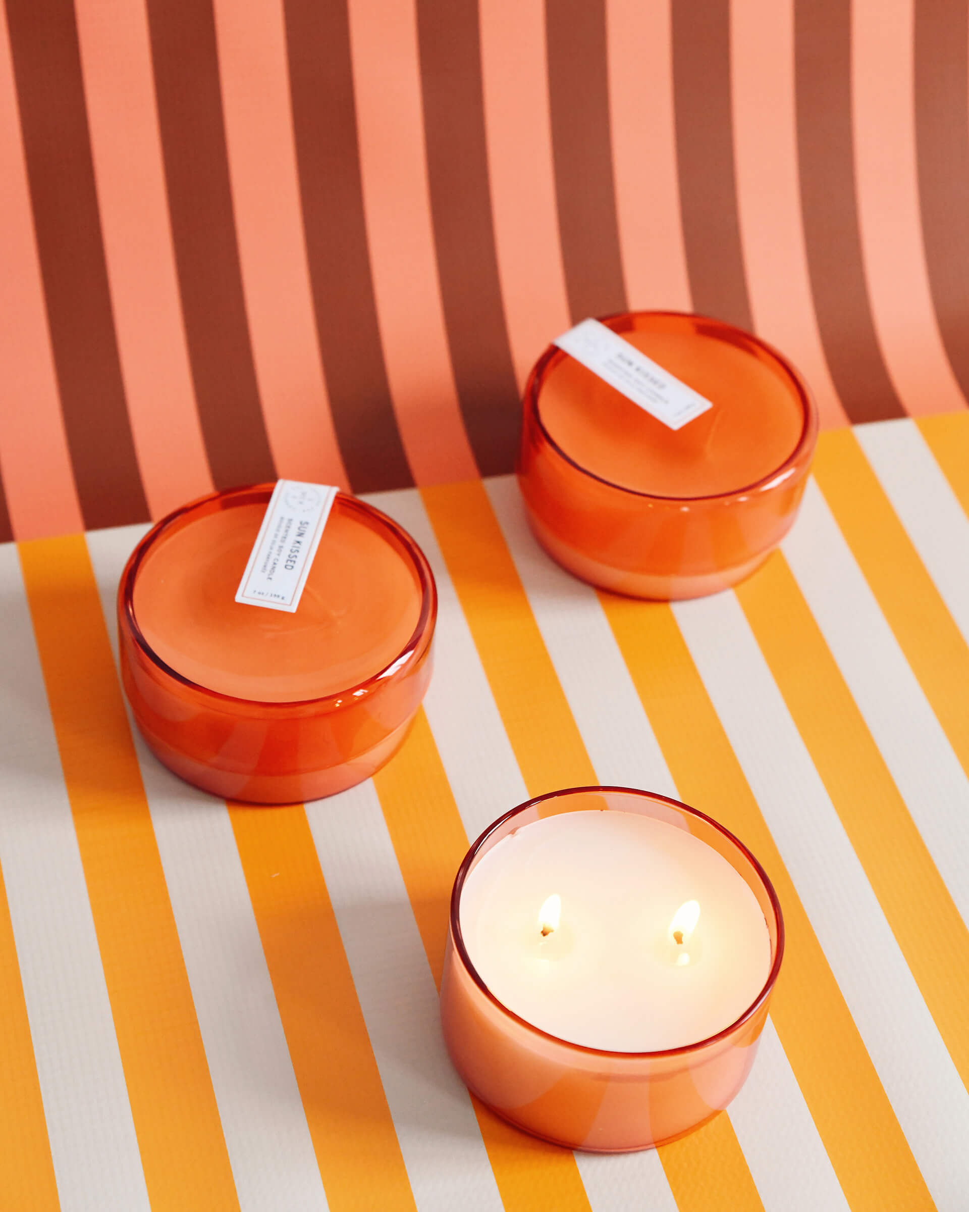 three 7 oz orange sun kissed canister candles on a orange and white striped background