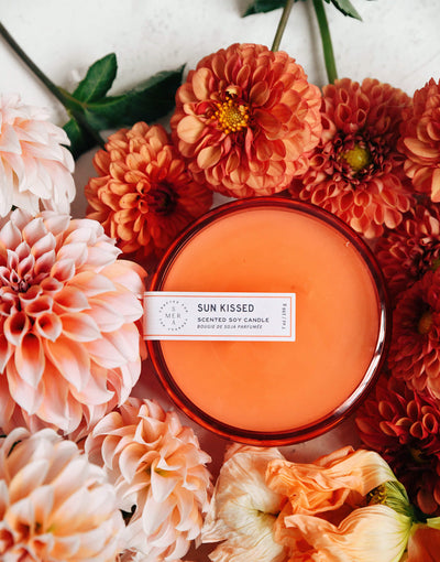 7 oz orange sun kissed canister candle surrounded by orange and whtie flowers 