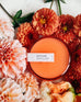 7 oz orange sun kissed canister candle surrounded by orange and whtie flowers 