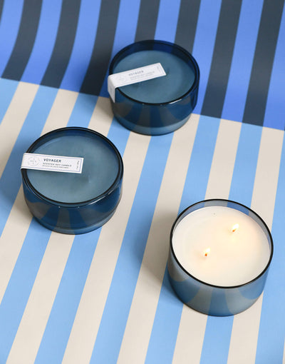 three 7 oz dark blue voyager canister candles on a blue and white striped background