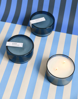 three 7 oz dark blue voyager canister candles on a blue and white striped background