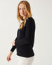 blonde female wearing black sweater standing sideways pulling down sleeve on a white background 