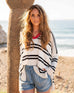 female wearing white and navy striped polo sweater with red collar standing near tree on beach