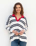 female wearing white and navy striped polo sweater with red collar leaning on white wall