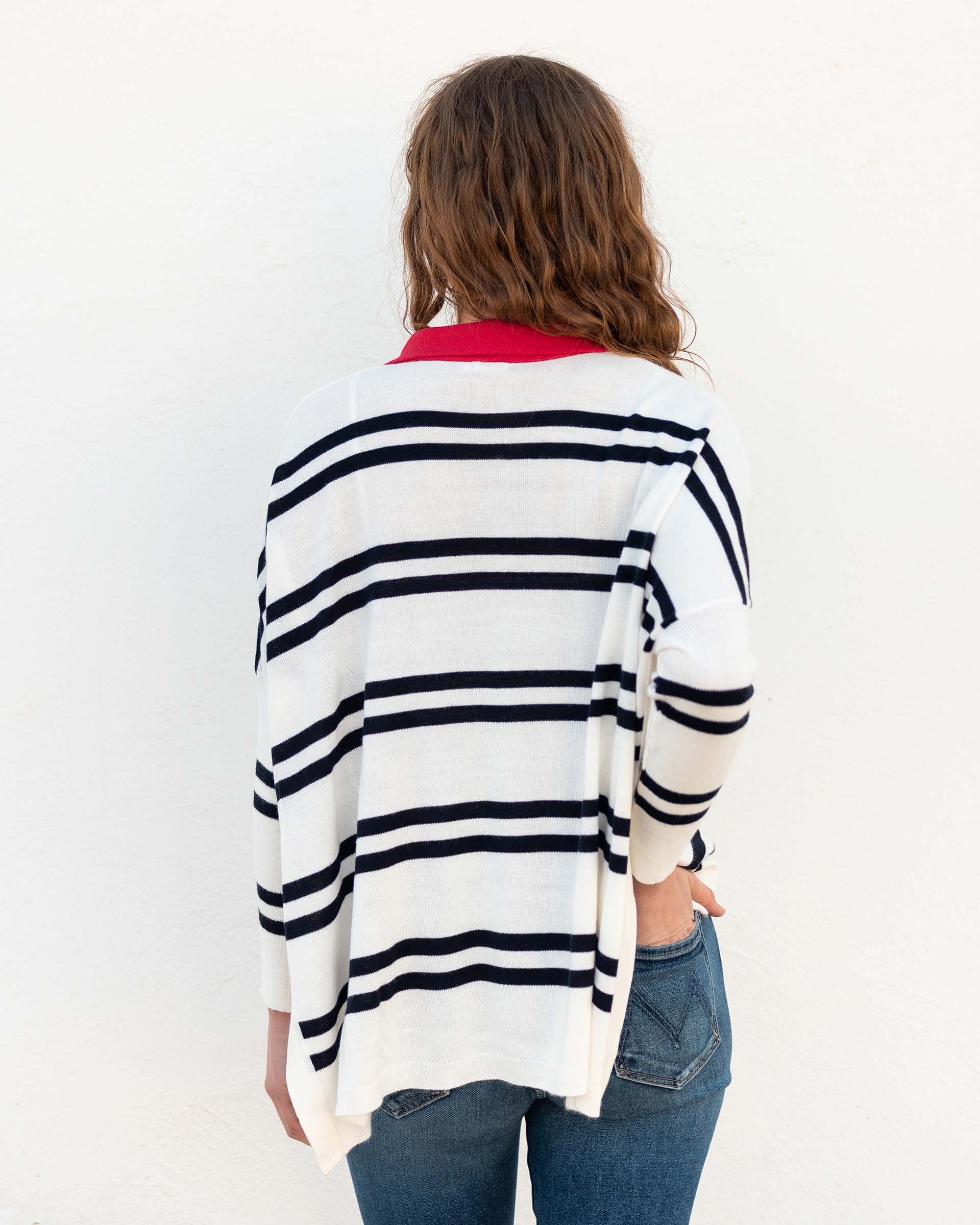 female wearing white and navy striped polo sweater with red collar backwards on white wall