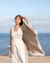 female wearing mink with white detail travel wrap blowing in the wind standing on the beach