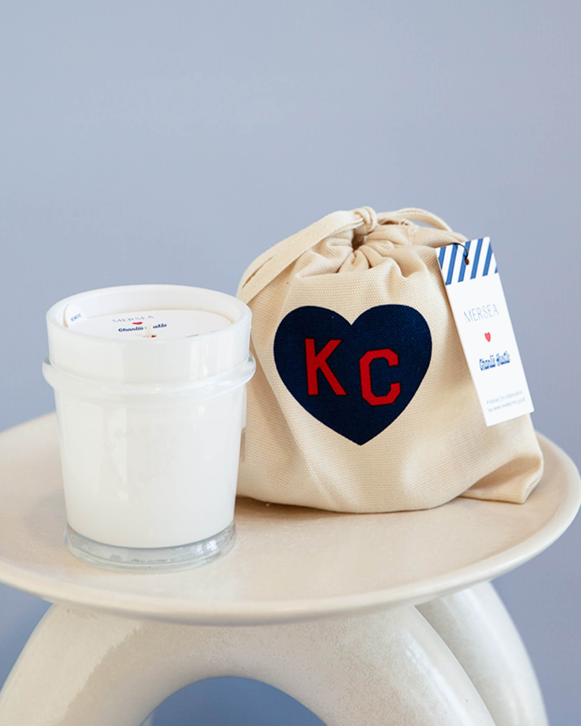mersea colab saltaire candle sitting next to KC inside heart on candle bag on stool