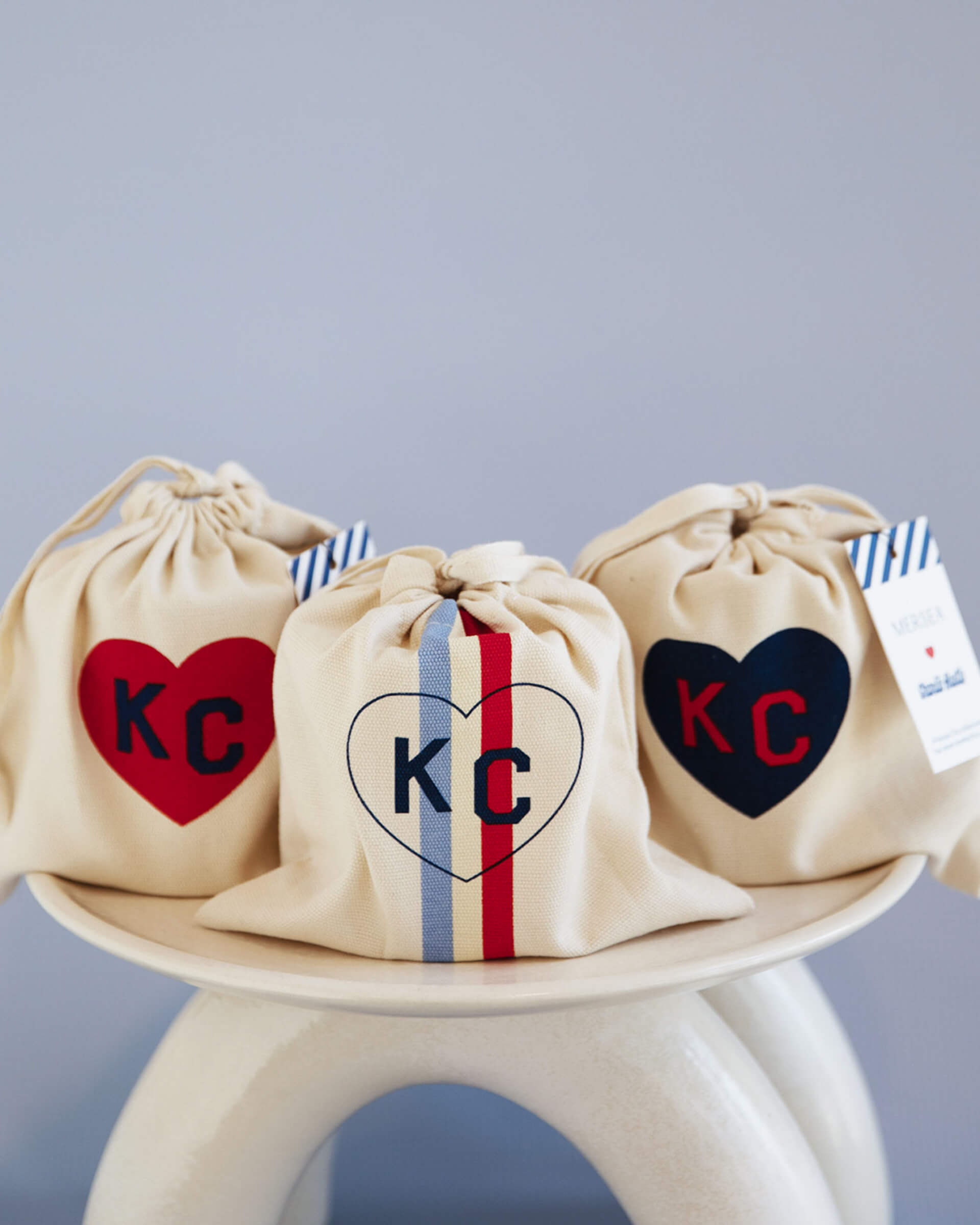 three designs of mersea colab saltaire candle with KC inside heart on candle bag on stool