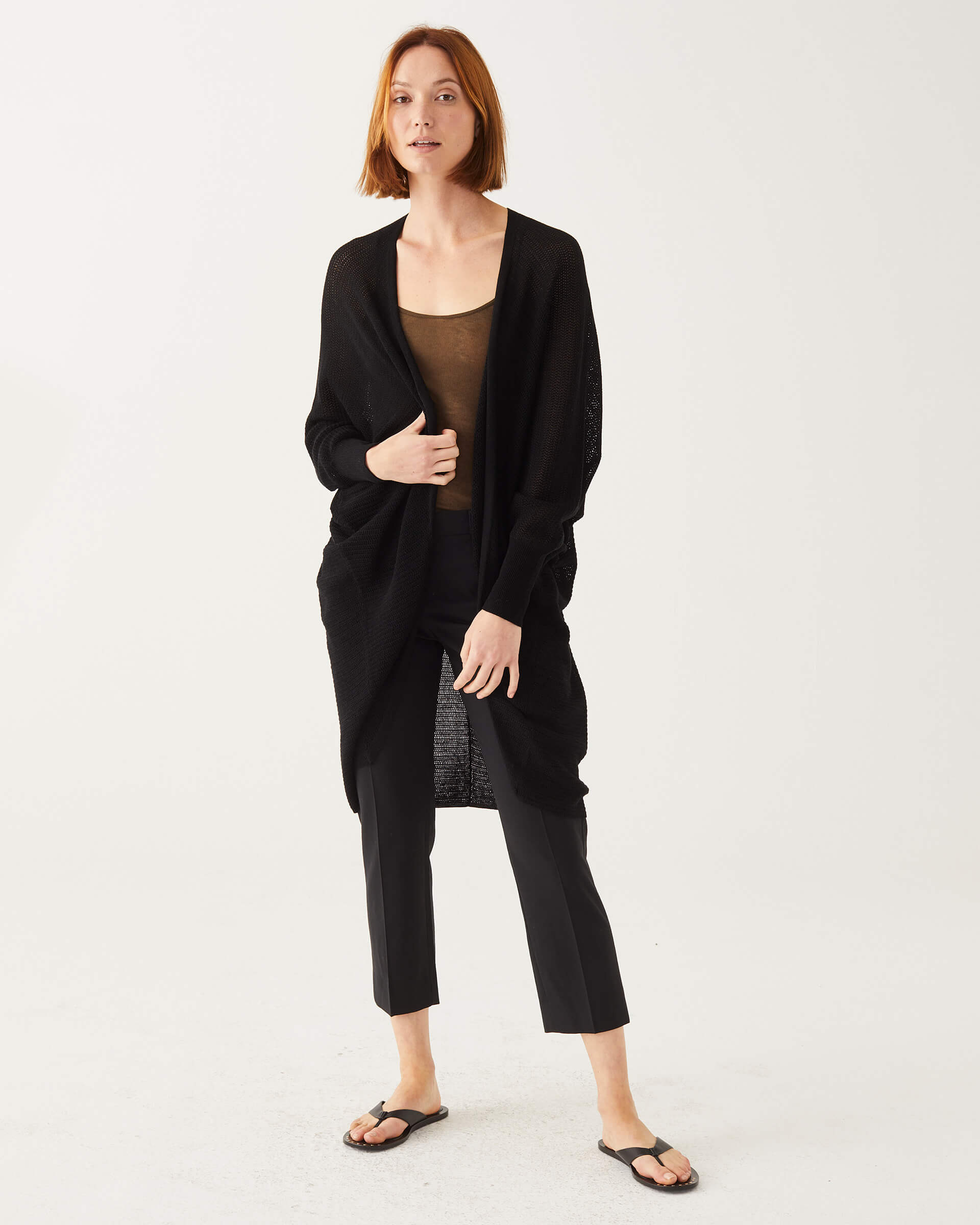 female putting on black cardigan with dolman sleeves on a white background