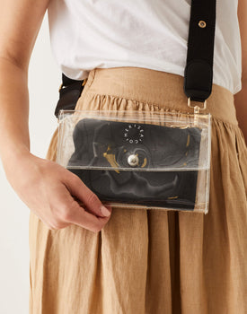 close up of female wearing crossbody clear bag with black straps over a shoulder with beige skirt