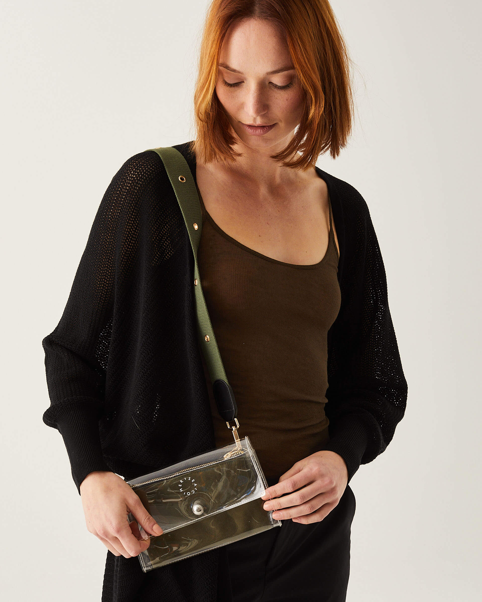 Female wearing black duster with crossbody clear bag over a shoulder with a green strap