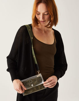 Female wearing black duster with crossbody clear bag over a shoulder with a green strap