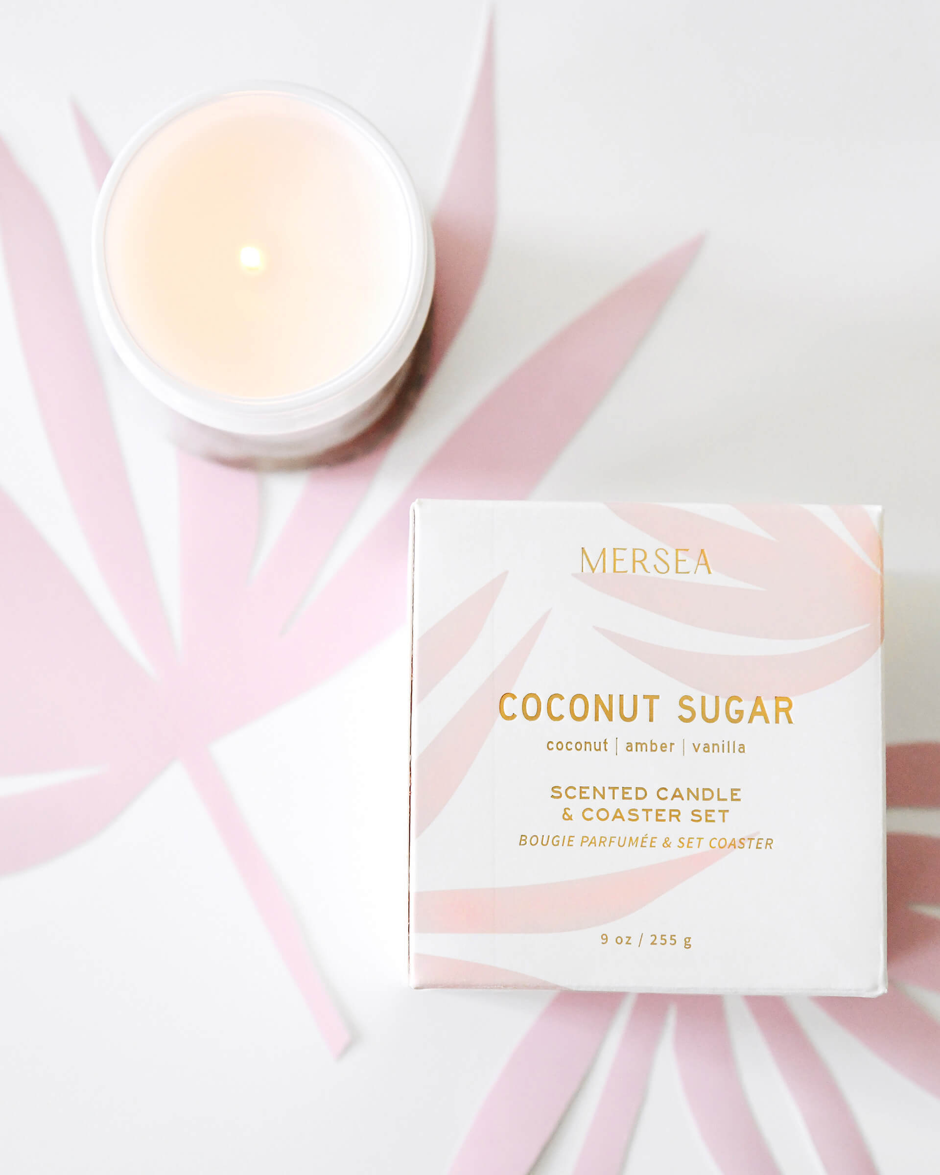 boxed coconut sugar candle with coaster and unboxed white candle on white and pink leaves background