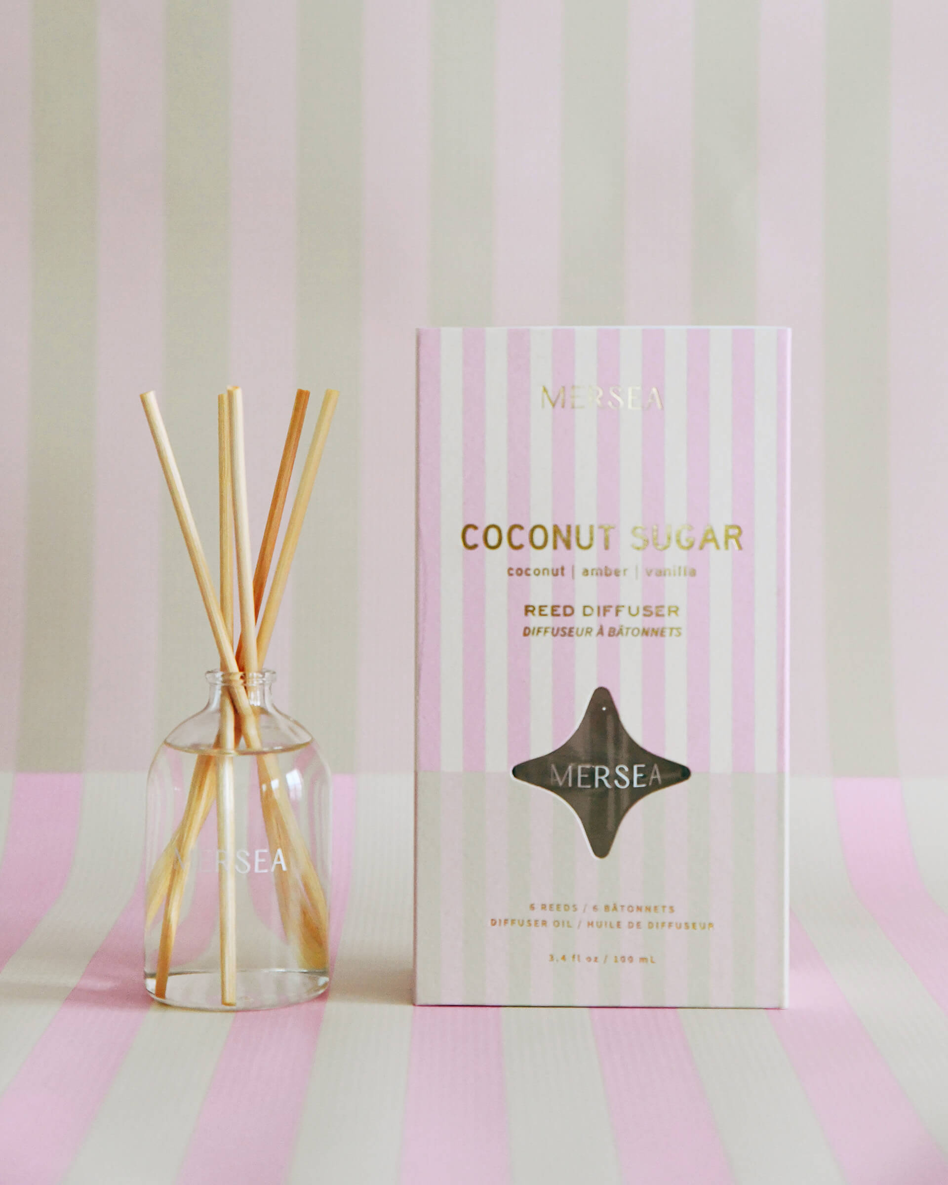 Coconut Sugar reed diffuser boxed in pink, green and white stripes on the same striped background 