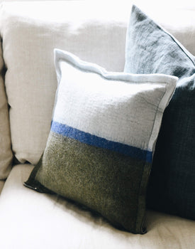 light blue and dark green felt wool pillow sitting on a neutral couch in front of a pillow