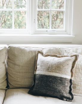 neutral and grey felt wool pillow with a white line across the middle sitting on a neutral couch