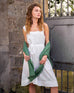 female wearing white A-line linen sundress with self-belt with green sweater standing near a gate 
