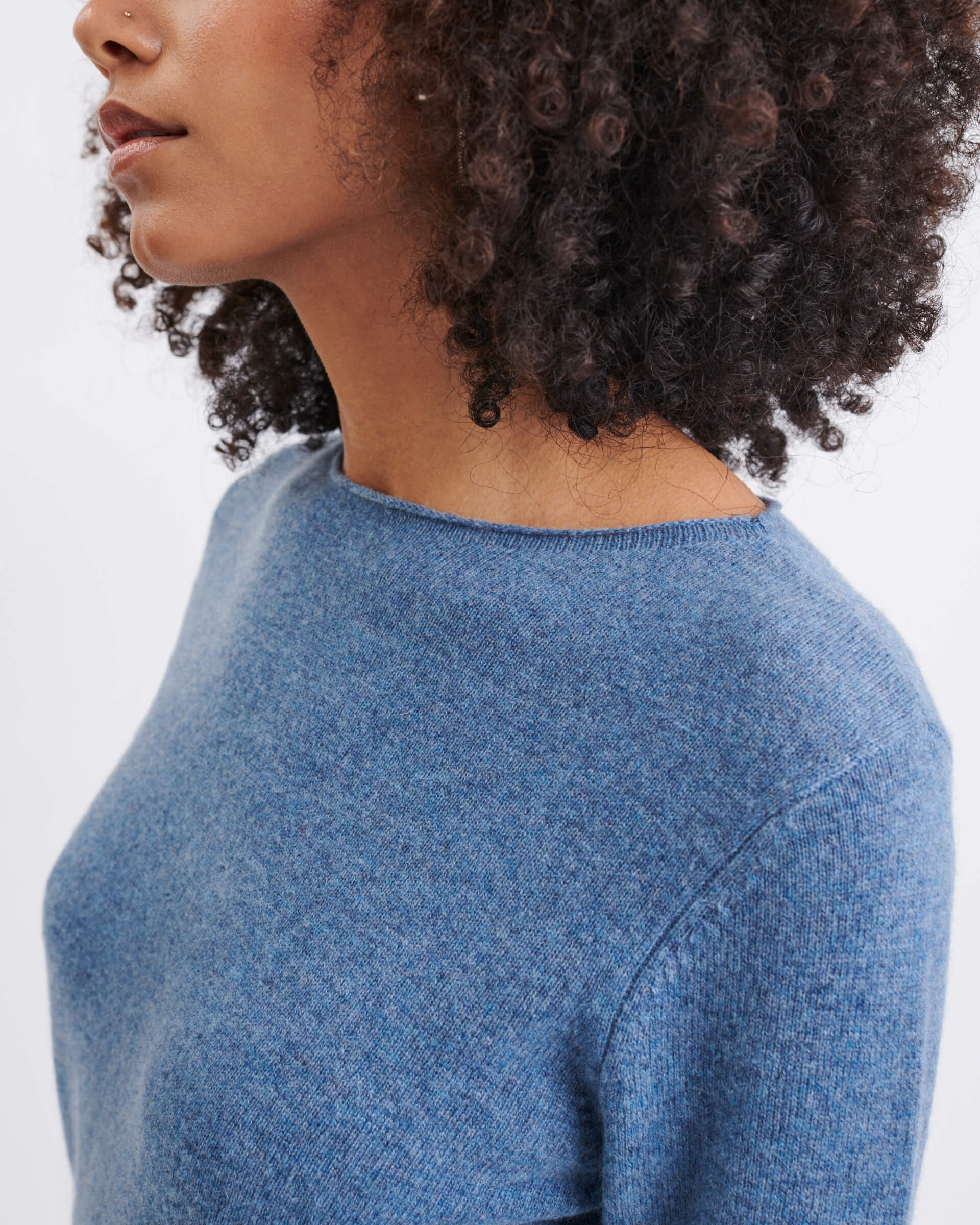 close up of dark blue sweater on female focused on crew neckline and rolled hem on white background