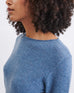 close up of dark blue sweater on female focused on crew neckline and rolled hem on white background