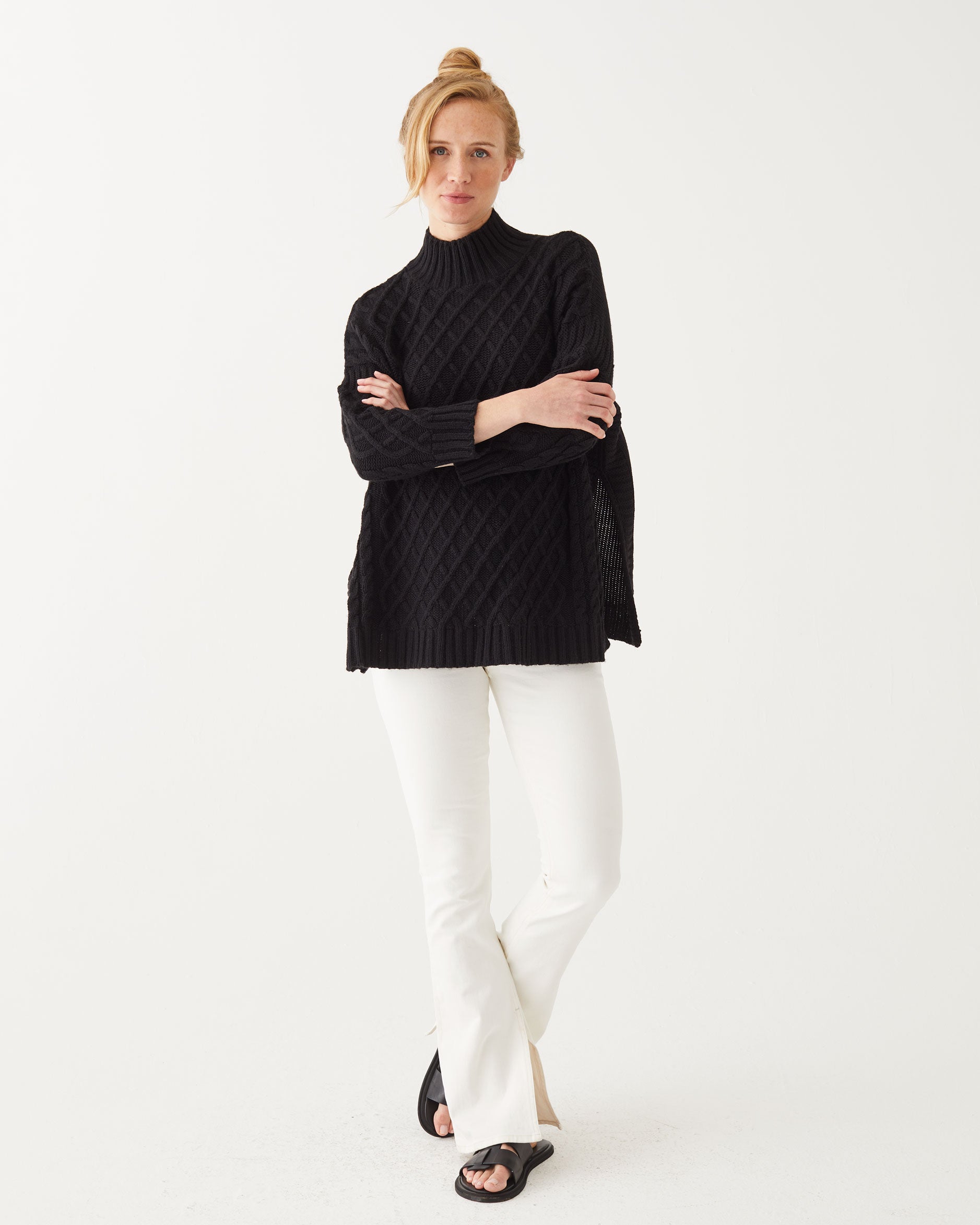 strawberry blonde female wearing black sweater standing with arms crossed on a white background