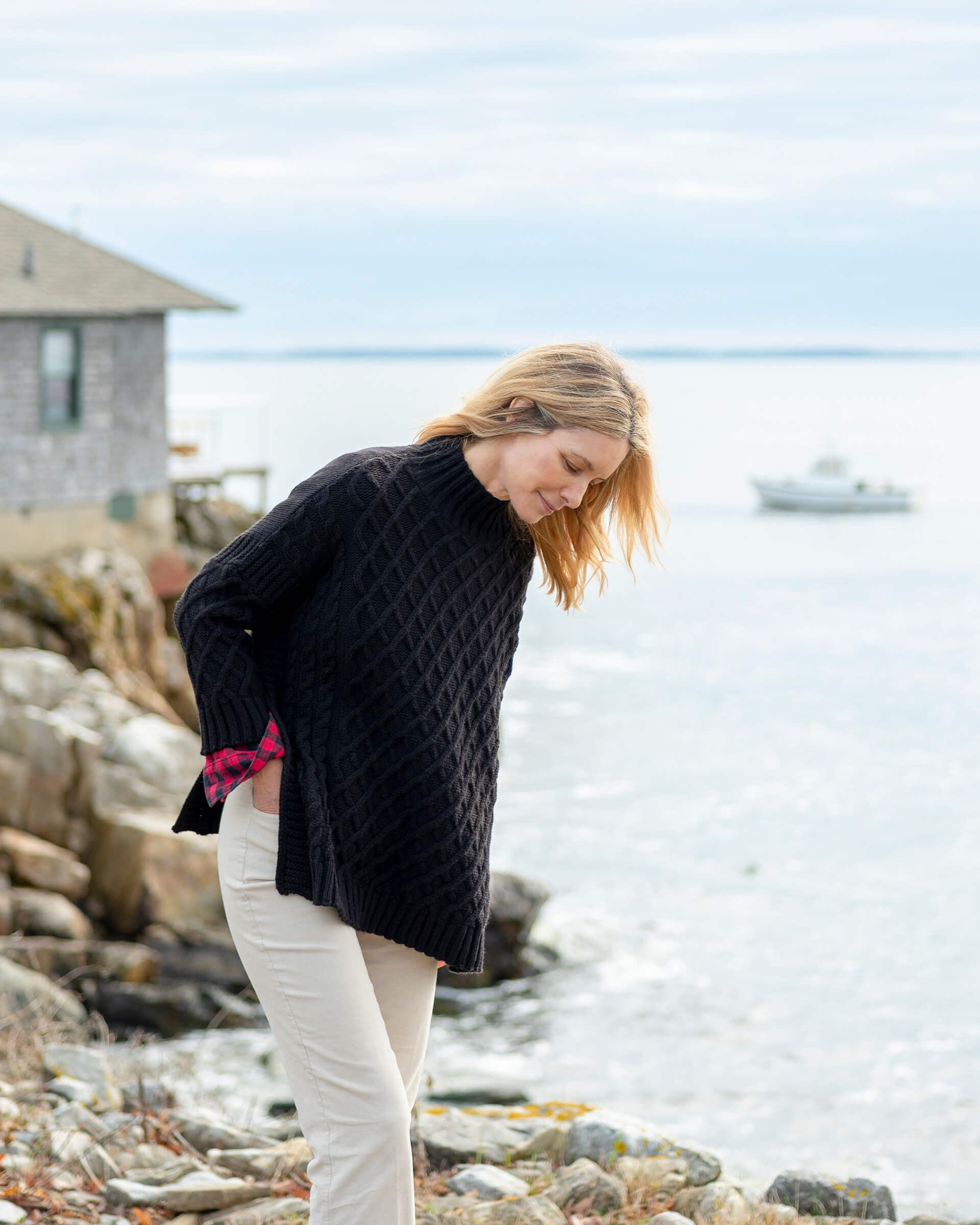 blonde female wearing black sweater standing on rocks near the ocean