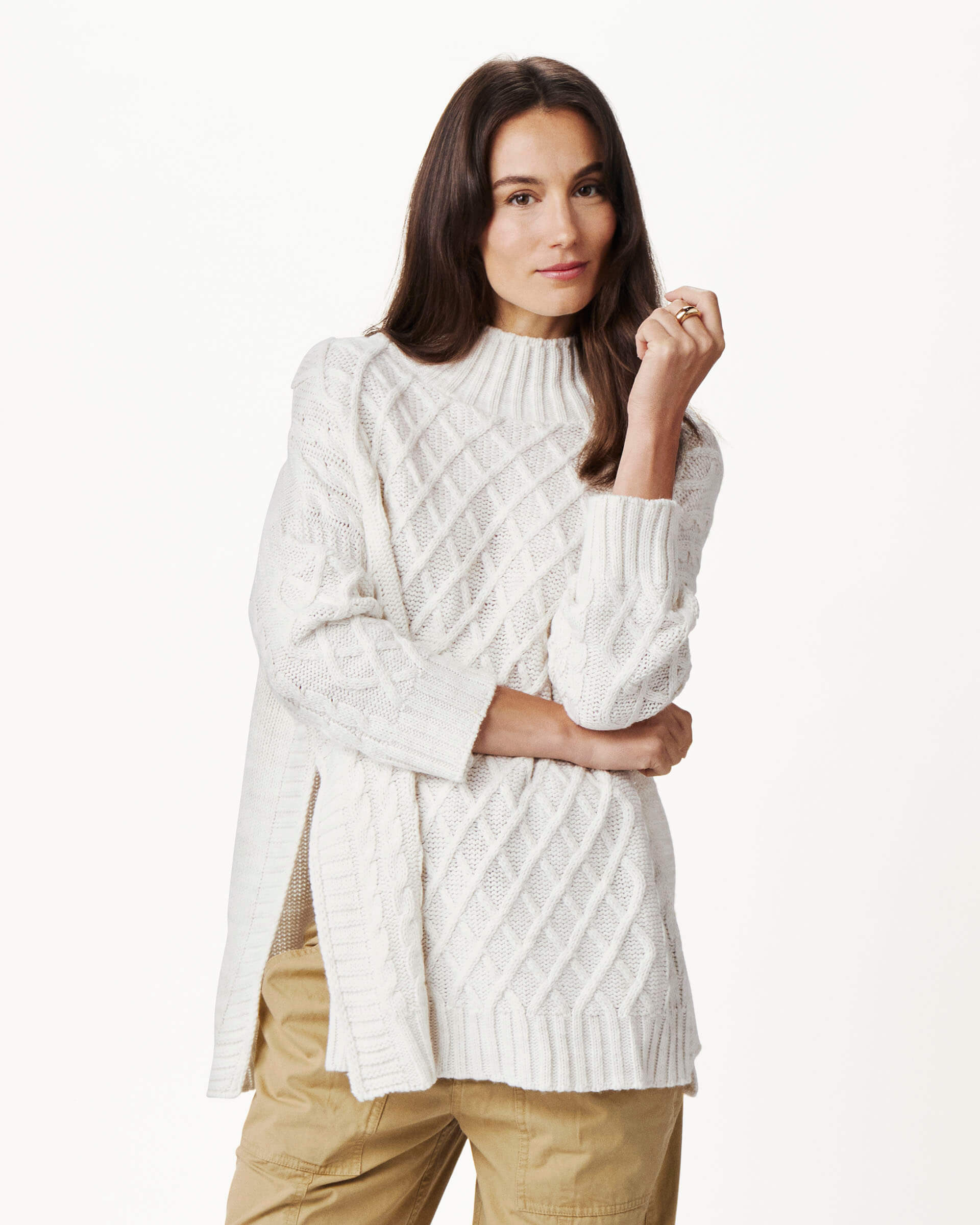 brunette female wearing white sweater with an arm holding her elbow on a white background