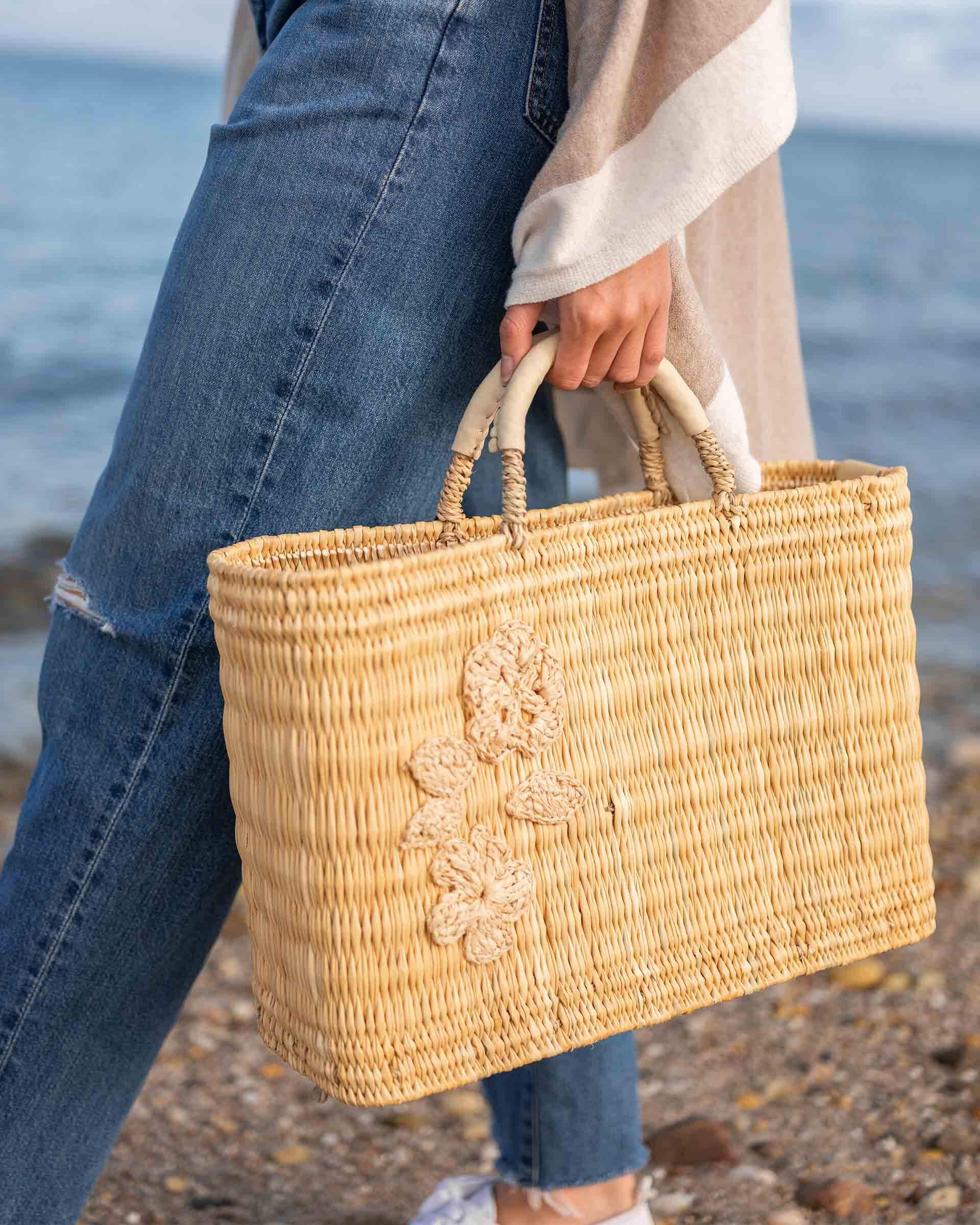 female holding medium sized straw basket with handwoven natural floral standing on beach