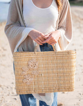 female holding medium sized straw basket with handwoven natural floral standing on beach