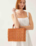 female wearing orange and beige small striped basket with red leather handles on a white background
