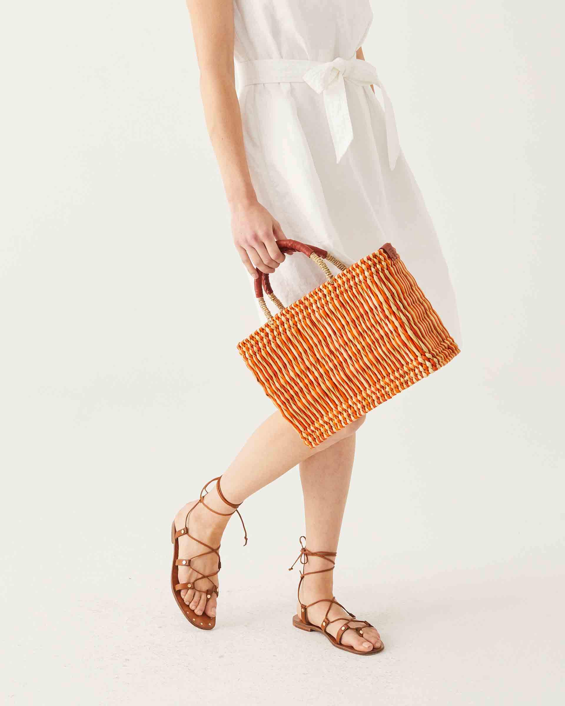 female walking with orange and beige small striped basket on a white background
