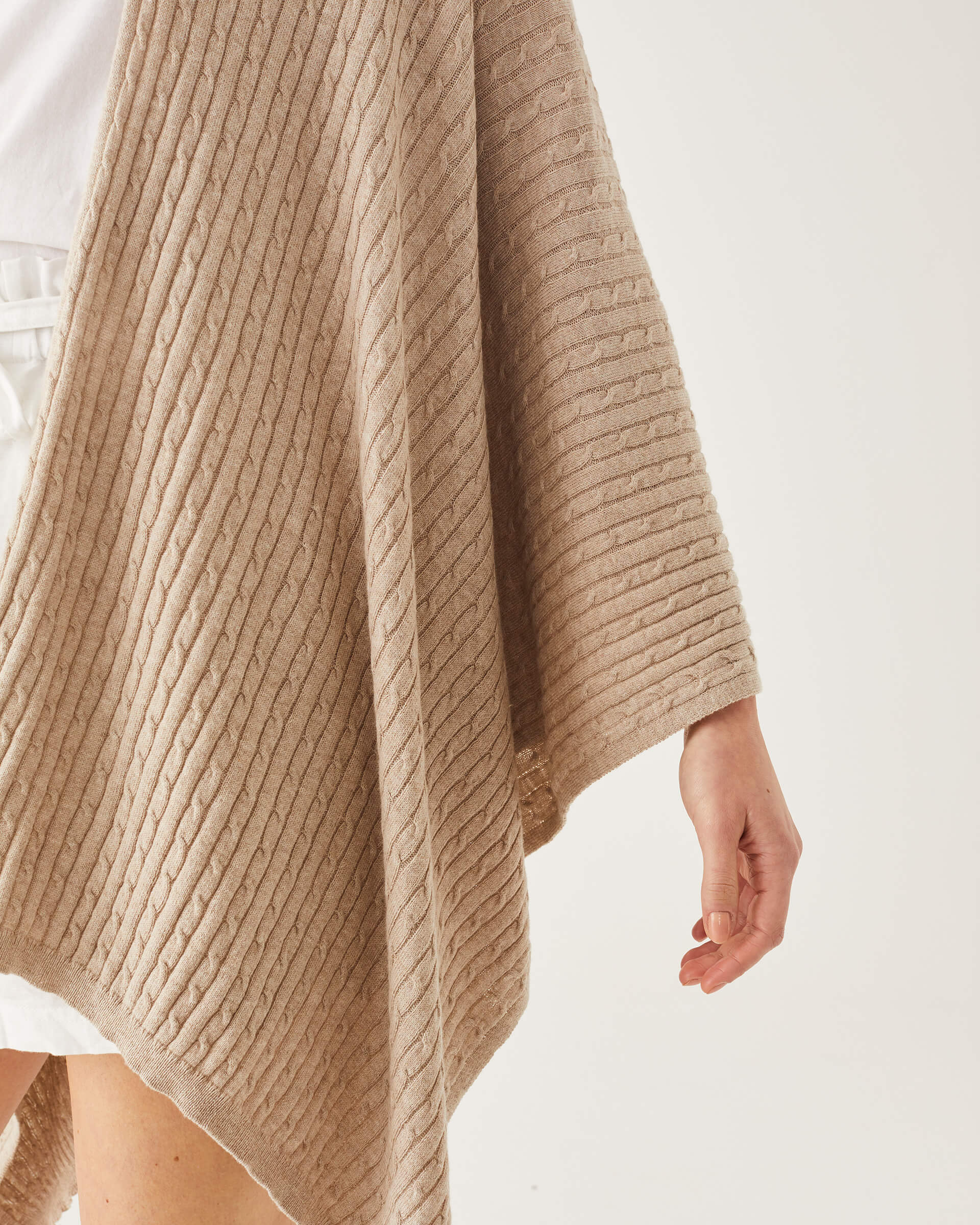 close up of female wearing light brown wrap with cable knit details on a white background
