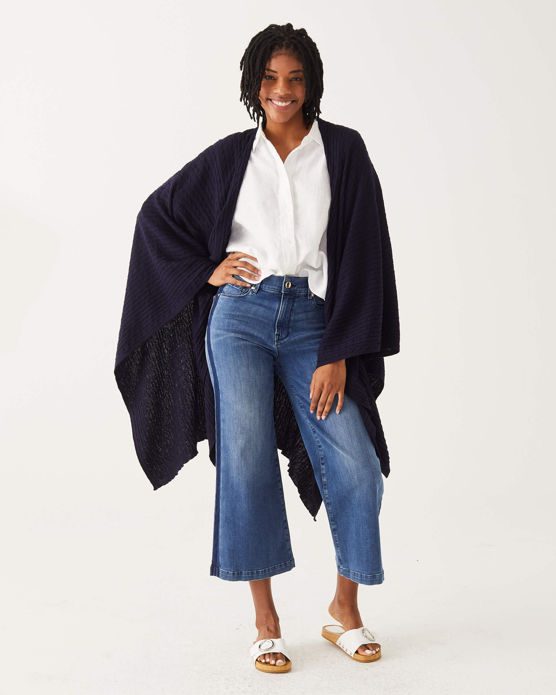female wearing navy cable knit wrap over her shoulders with a hand on a hip on a white background