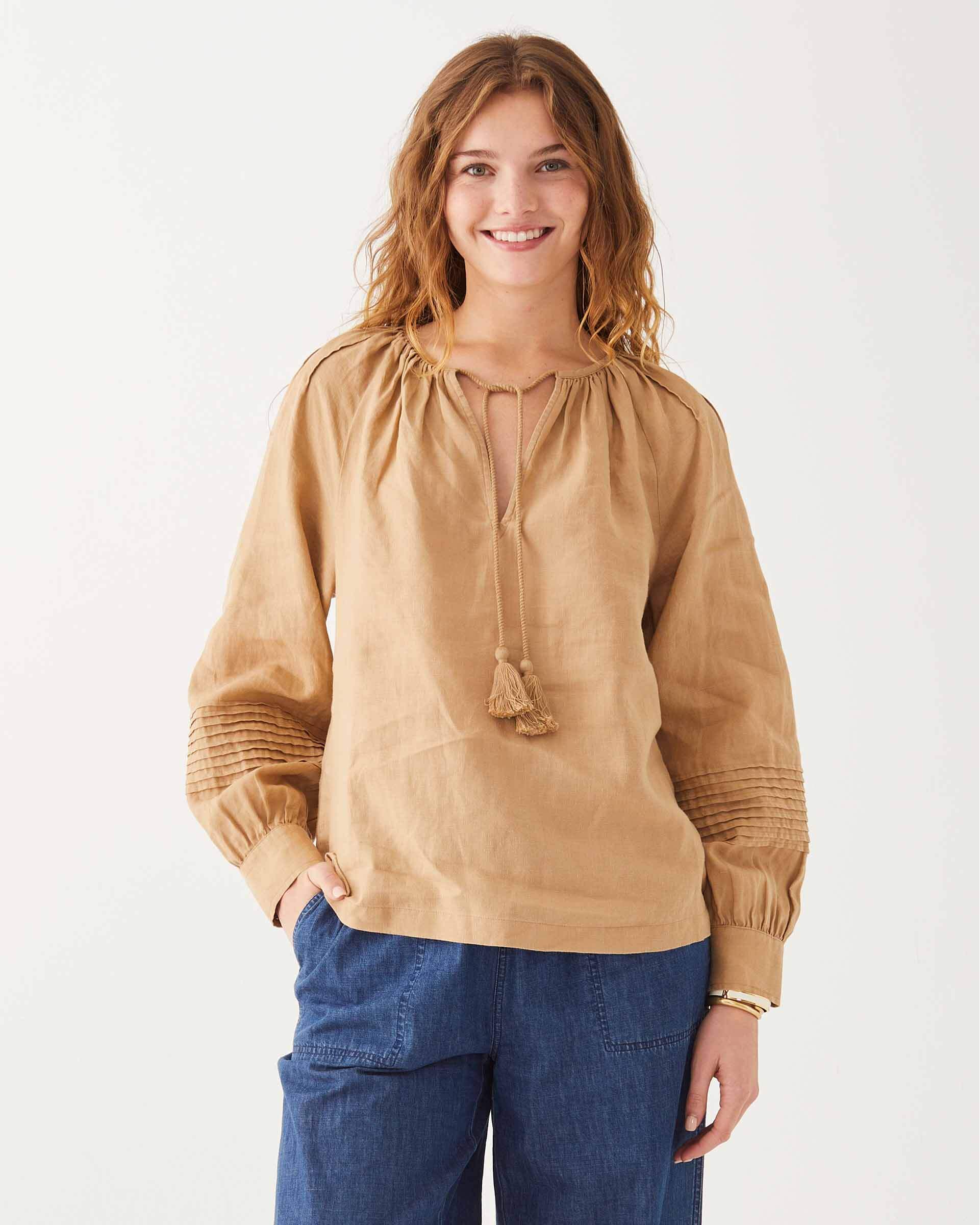 female wearing tan linen blouse with v-neck, tassels, and side slits on a white background