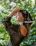 female wearing black scarf with brown vine pattern in her hair standing sideways in the trees