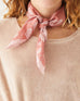 female wearing pink scarf with light pink vine pattern tied around her neck on a white background