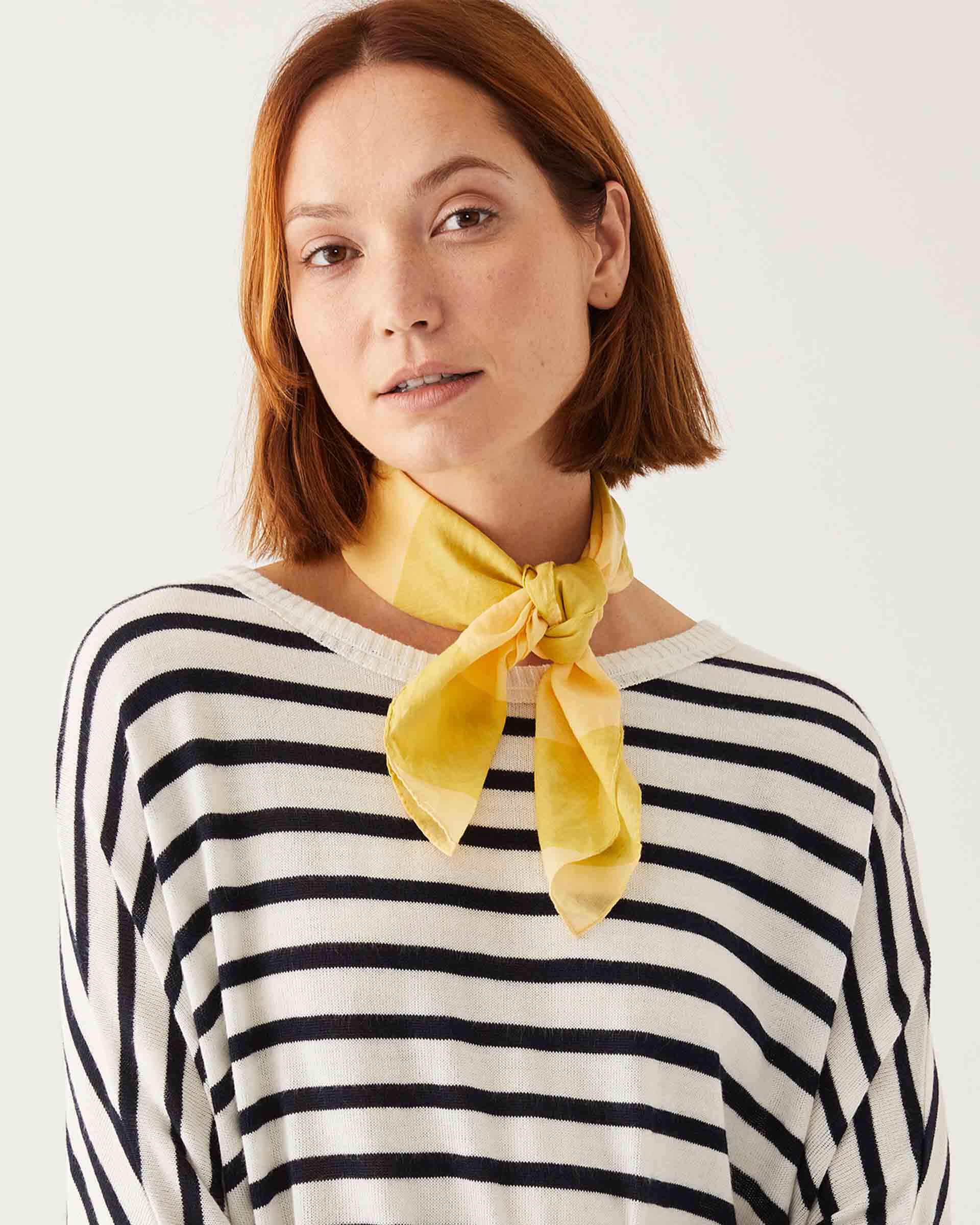 female wearing striped sweater with a yellow striped scarf around her neck on a white background